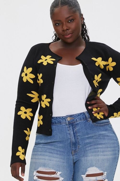 Model wears black cardigan with yellow flowers with a white top and midwash jeans