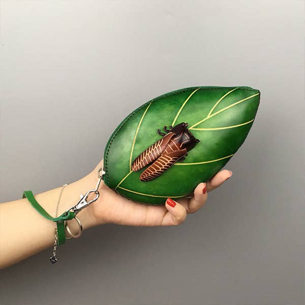 a hand holding the leaf clutch with a cicada bug in the center of it 