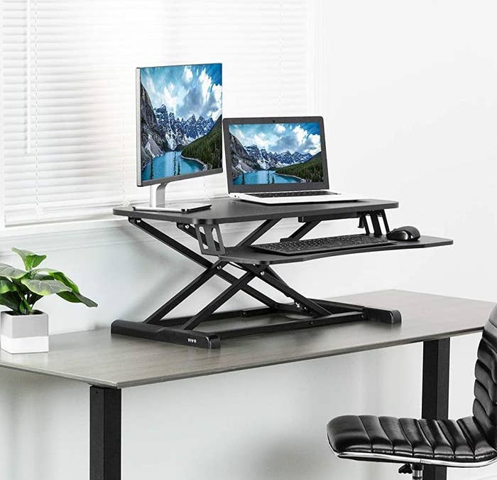A standing desk attachment on a desk next to an office chair 