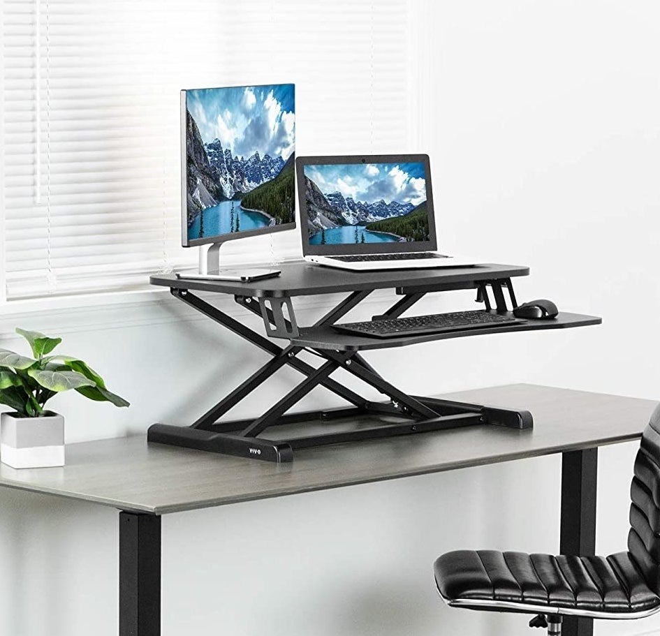 A standing desk attachment on a desk next to an office chair 
