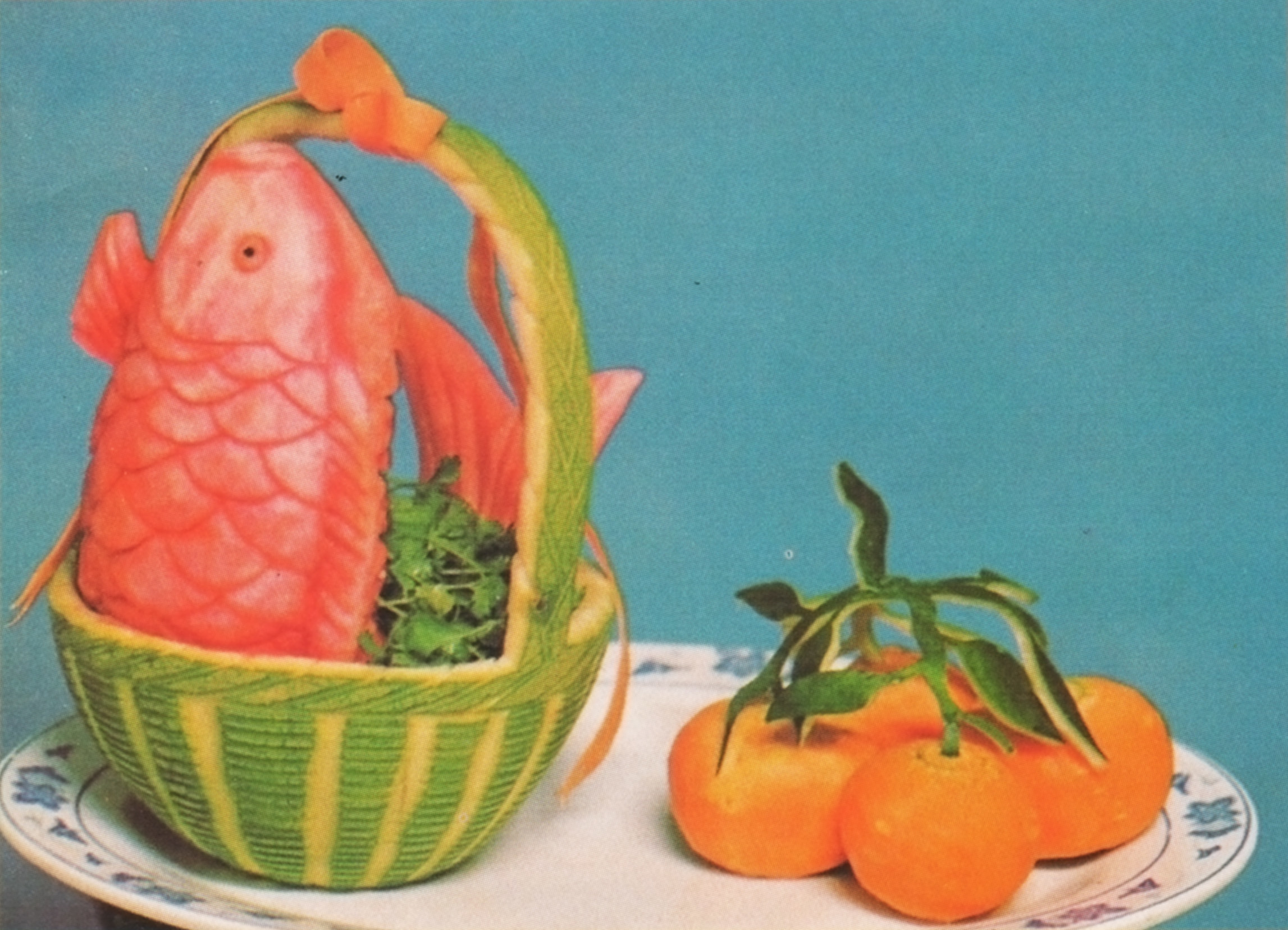 A fish in a basket made of  a carved gourd with oranges next to it on a plate