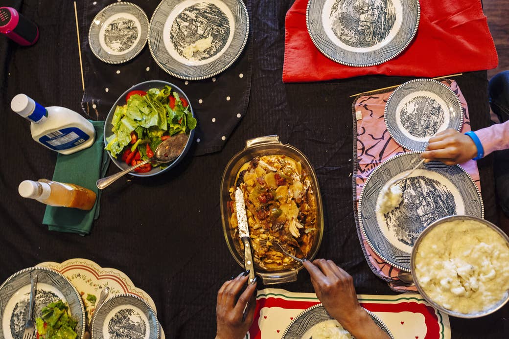 An overhead view of a tabletop covered in food dishes with hands reaching in to eat
