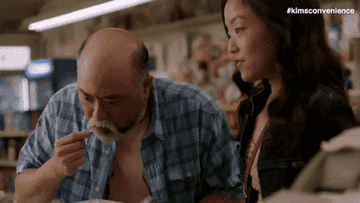 Appa and Janet from Kim&#x27;s Convenience Store gif with Appa taking a bite of something and widening his eyes in happy surprise