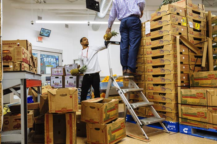 Two men in a grocery stockroom passing pineapples to each other