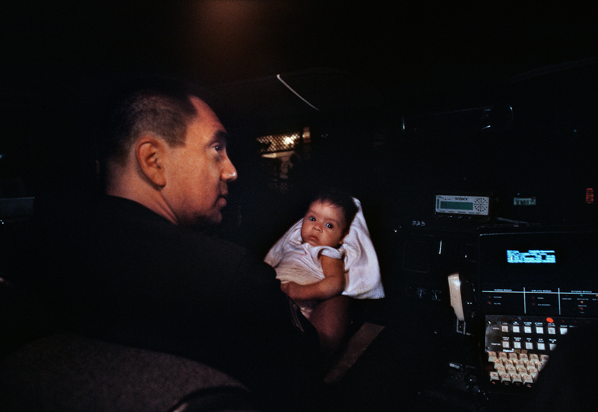 A cop holds a baby in a car at night