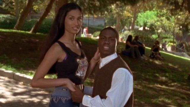 Kevin Hart in a sweater vest holding a tall woman&#x27;s hand on a college campus 