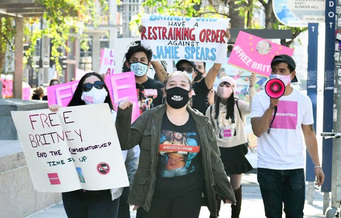 Several protesters walking down a street holding signs calling for the end of Britney's conservatorship