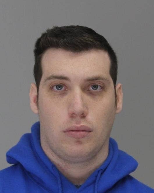 A mugshot of a white man in a blue hoodie