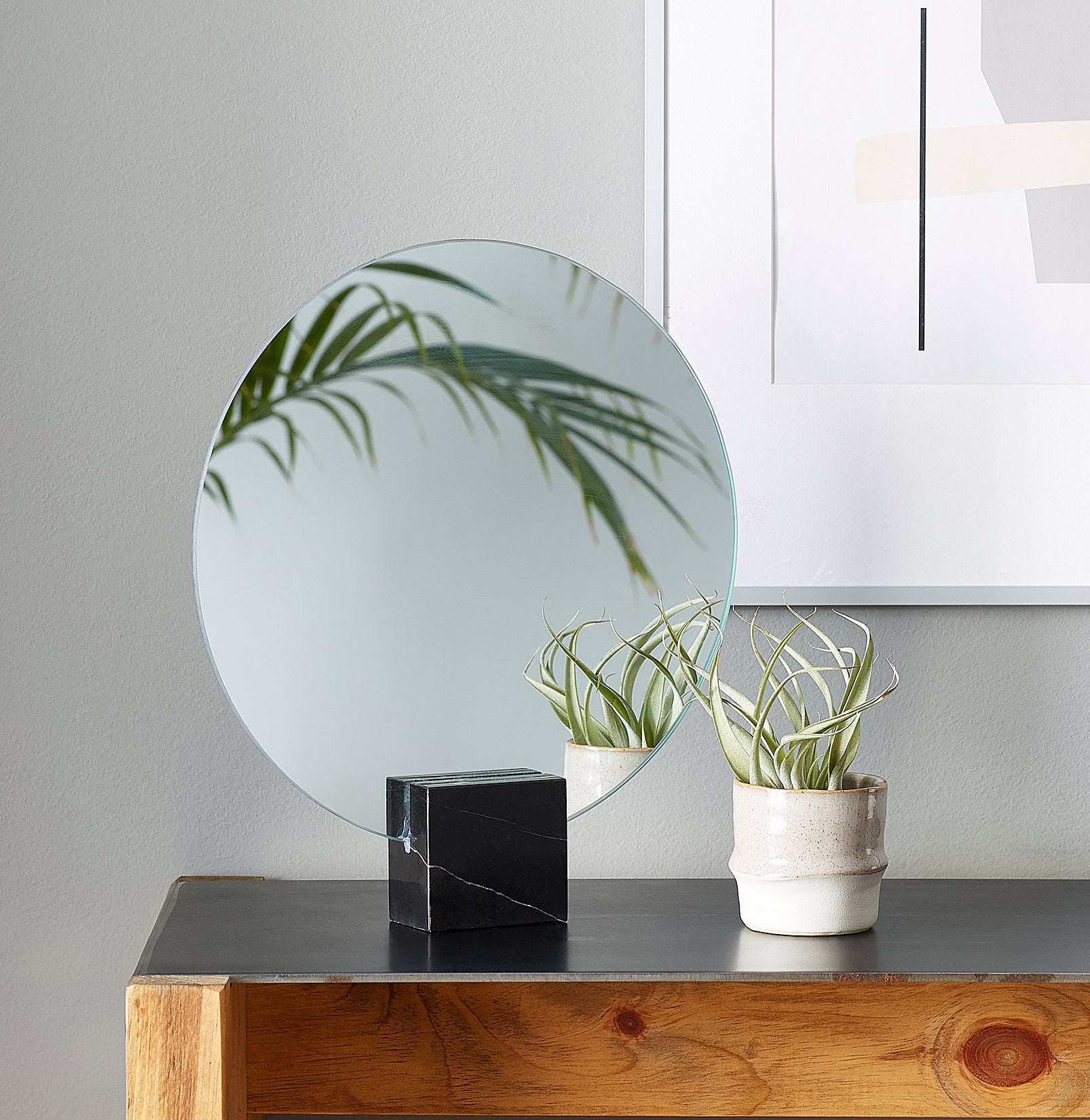 A round mirror sitting in a marble cube next to a small plant 
