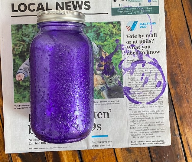 A spray painted mason jar is placed on a piece of newspaper. 