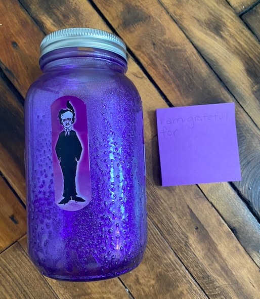 A spray painted mason jar is placed next to a stack of Post-It notes on a hardwood floor .