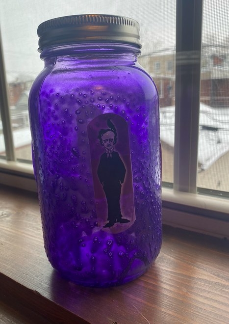 A spray painted mason jar with Edgar Allan Poe Band-Aids is sitting on a windowsill. 