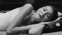A woman smirks as she lays on her side wearing a tank top. 