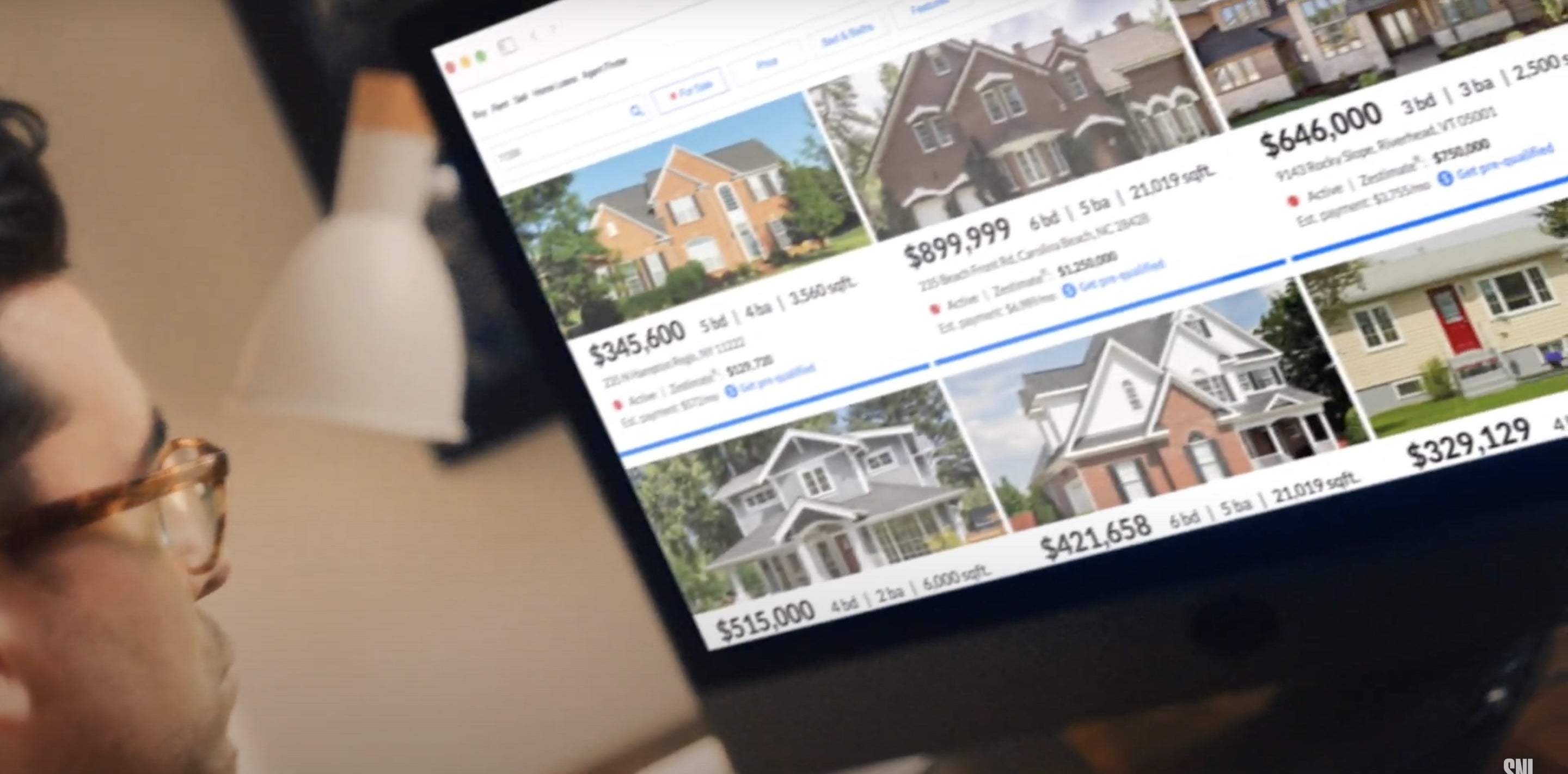 A man looks at a screen filled with Zillow listings 