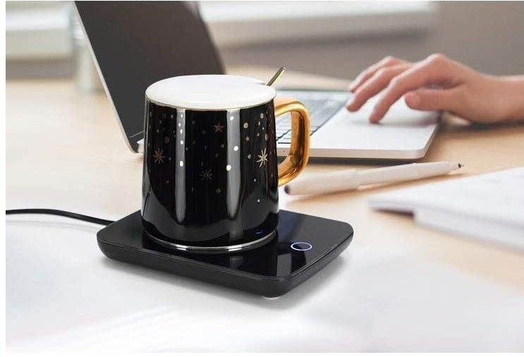 A mug heater next to a person using a laptop
