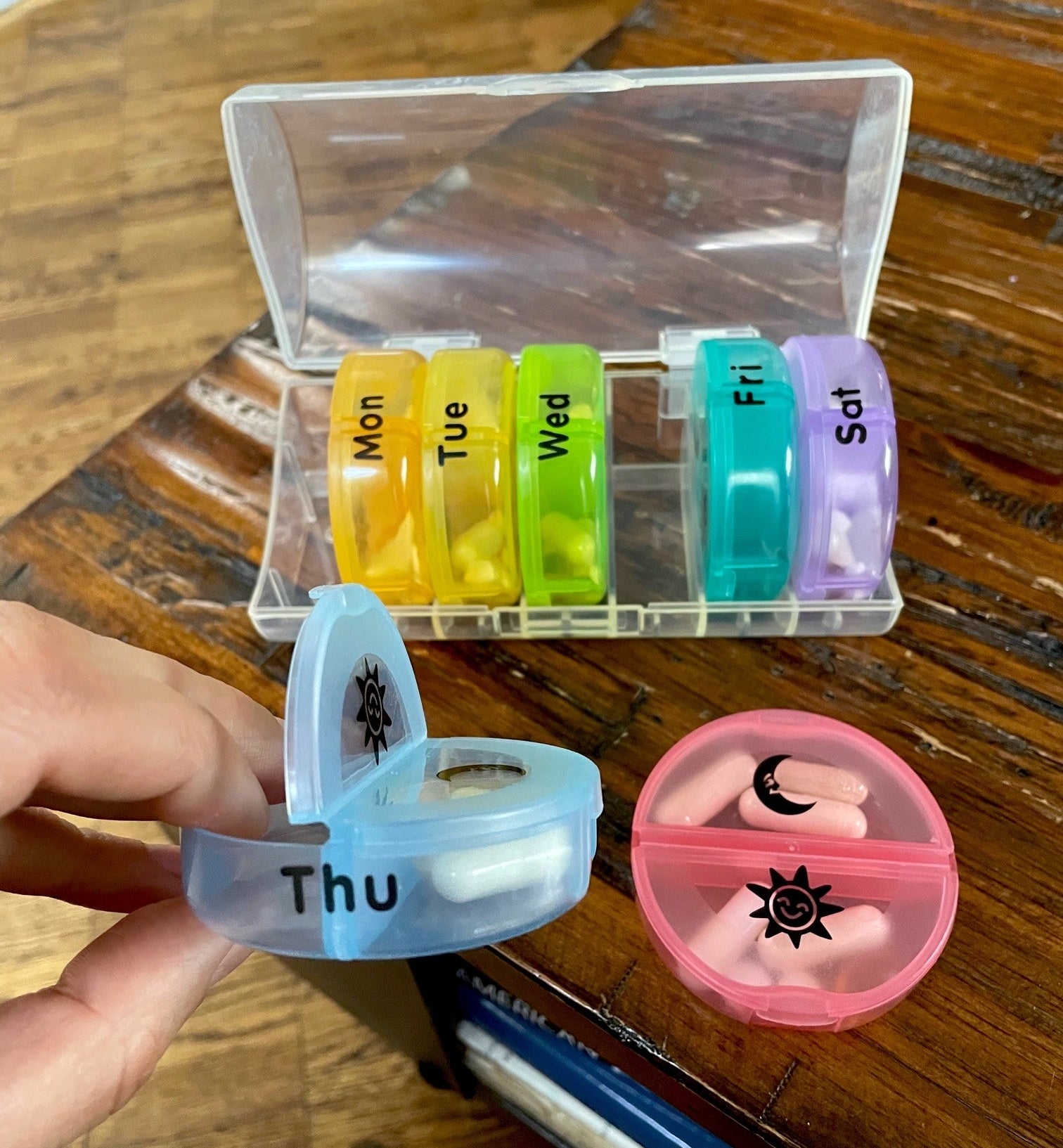 A person holding one of the pill containers in front of the whole pill storage box