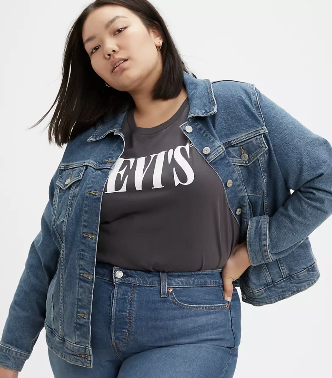Model is wearing a black shirt with a denim jacket over it and denim jeans