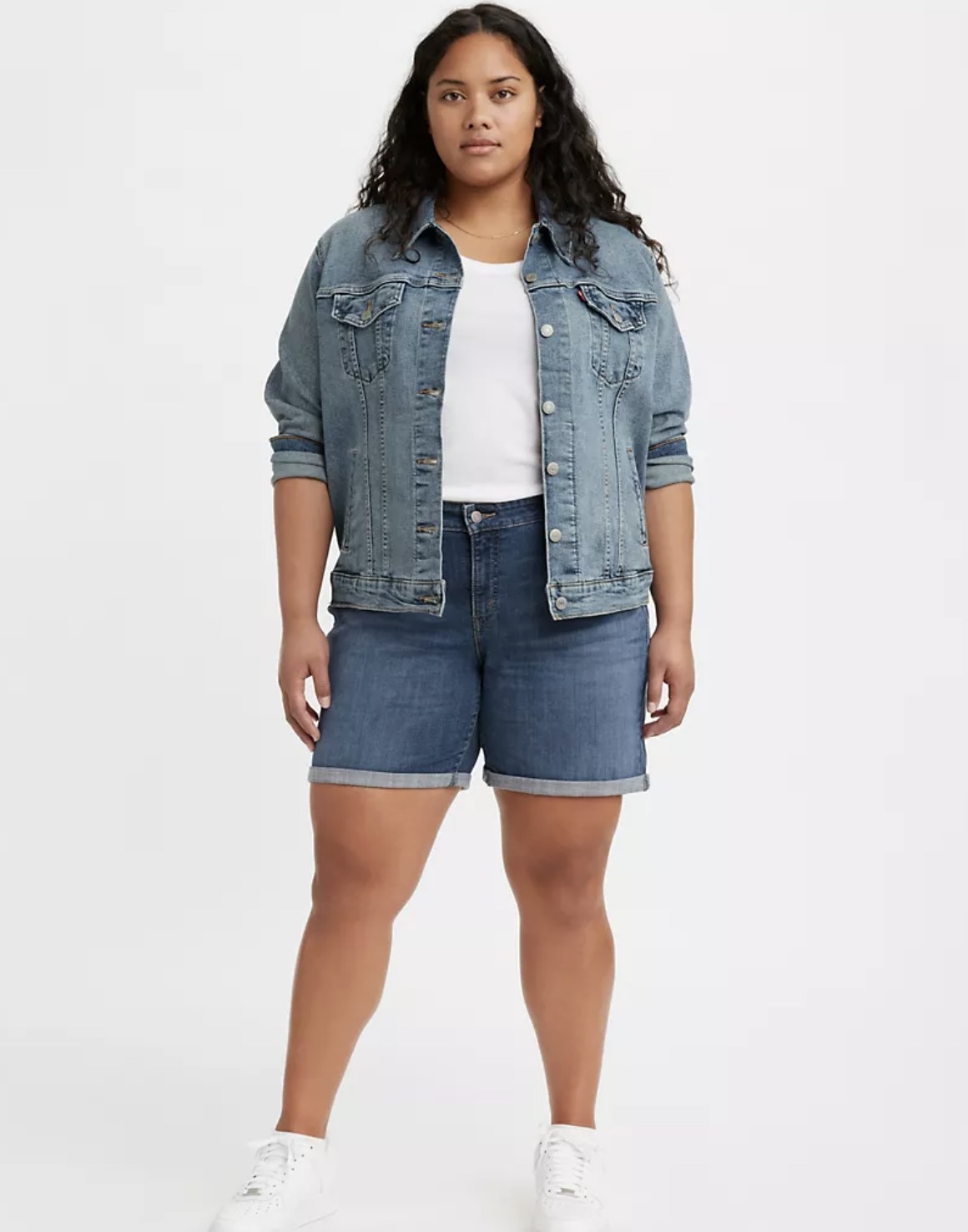 Model is wearing a white top, denim jacket, and denim shorts