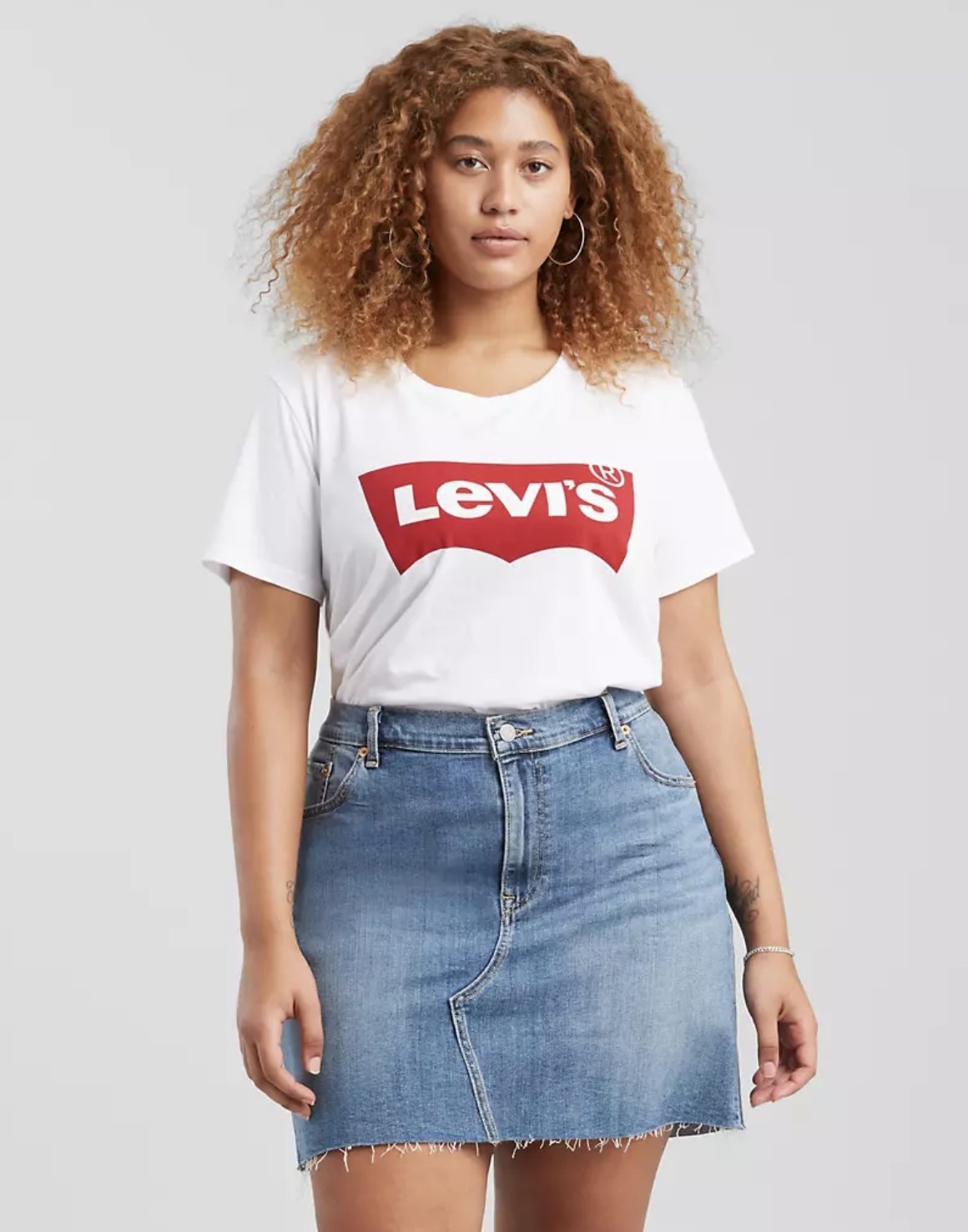 Model is wearing white tee with the Levi&#x27;s logo and a denim skirt