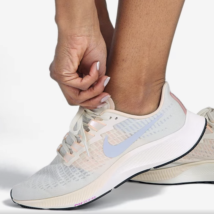 Model laces up light pink, blue, and gray running sneakers