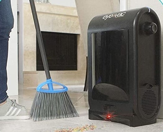 A person sweeps debris underneath the touchless vacuum, which sucks all the debris up