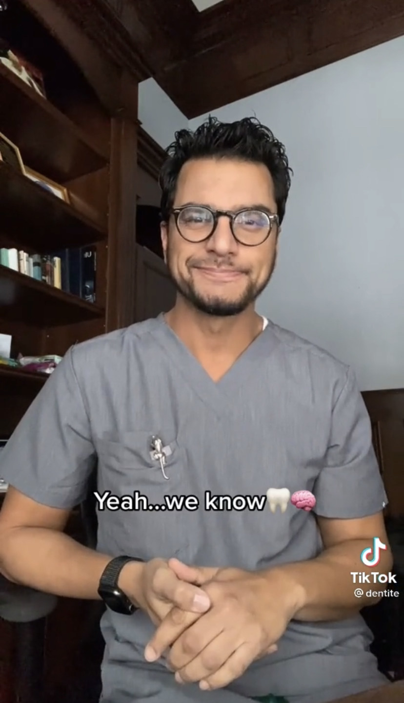 Dr. Huzefa Kapadia wearing his eyeglasses and scrubs in an office with the caption &quot;Yeah...we know [tooth emoji, brain emoji]