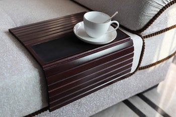 A wooden tray folded along the edge of a couch with a mug on top of it 