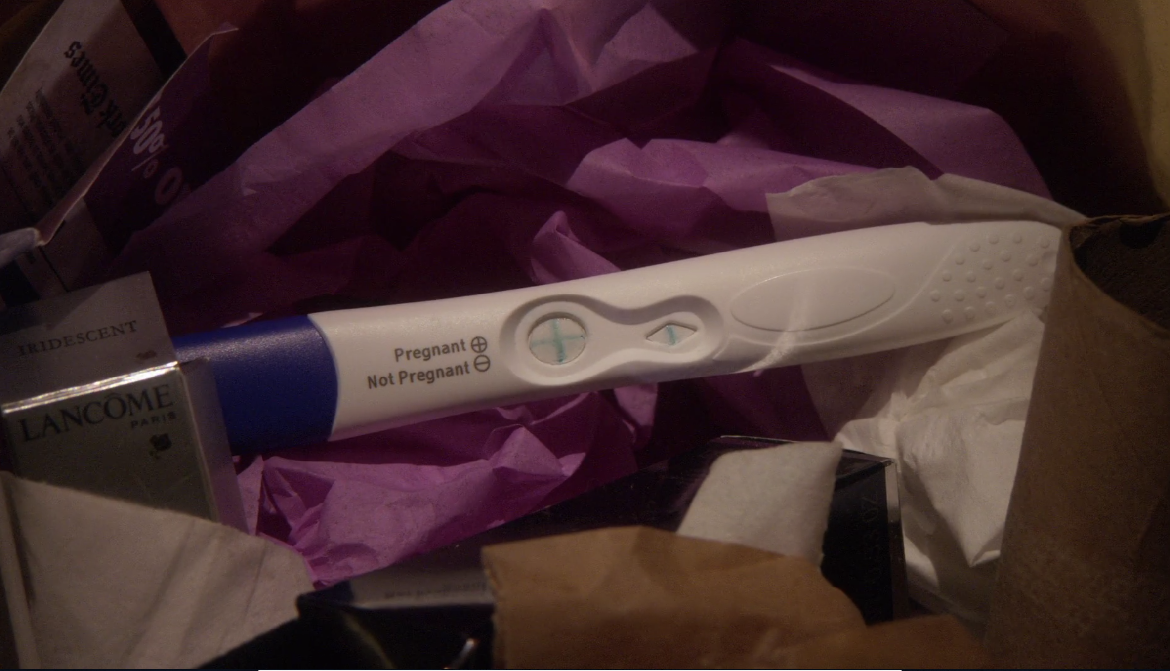 a positive pregnancy test faceup in the trash