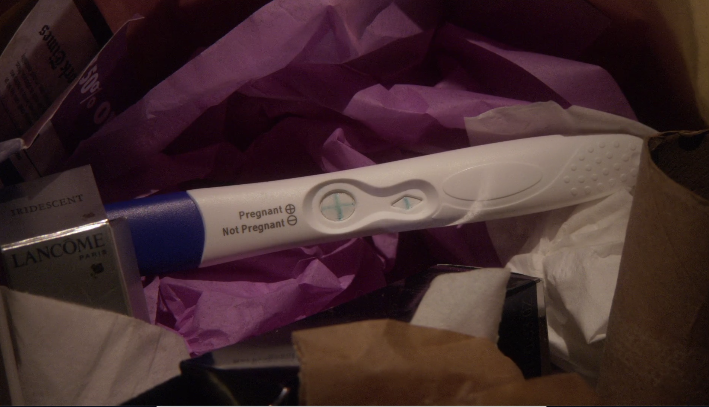 a positive pregnancy test face up in the trash