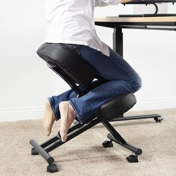 Model with their knees resting on a support bar and bottom resting on a pad in a chair low to the ground