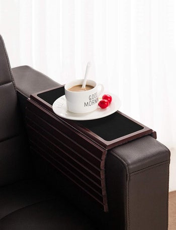 Same tray folded over a skinnier couch chair with a mug on it 