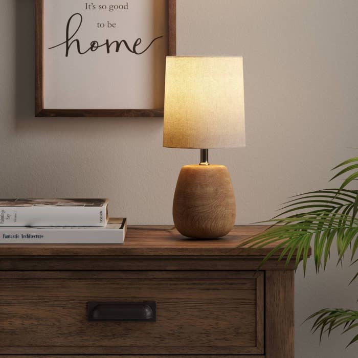 The lamp, which has a small, rounded base and a light-colored drum shade, in &quot;natural oak&quot;