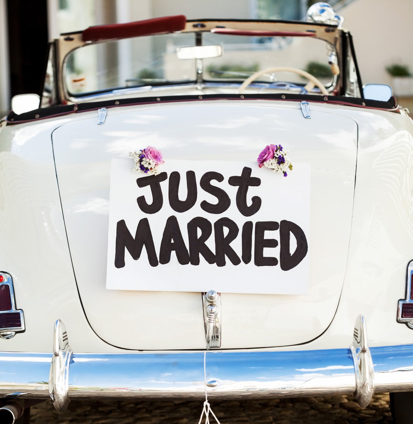 A &quot;Just Married&quot; sign and cans attached to convertible car&#x27;s trunk.