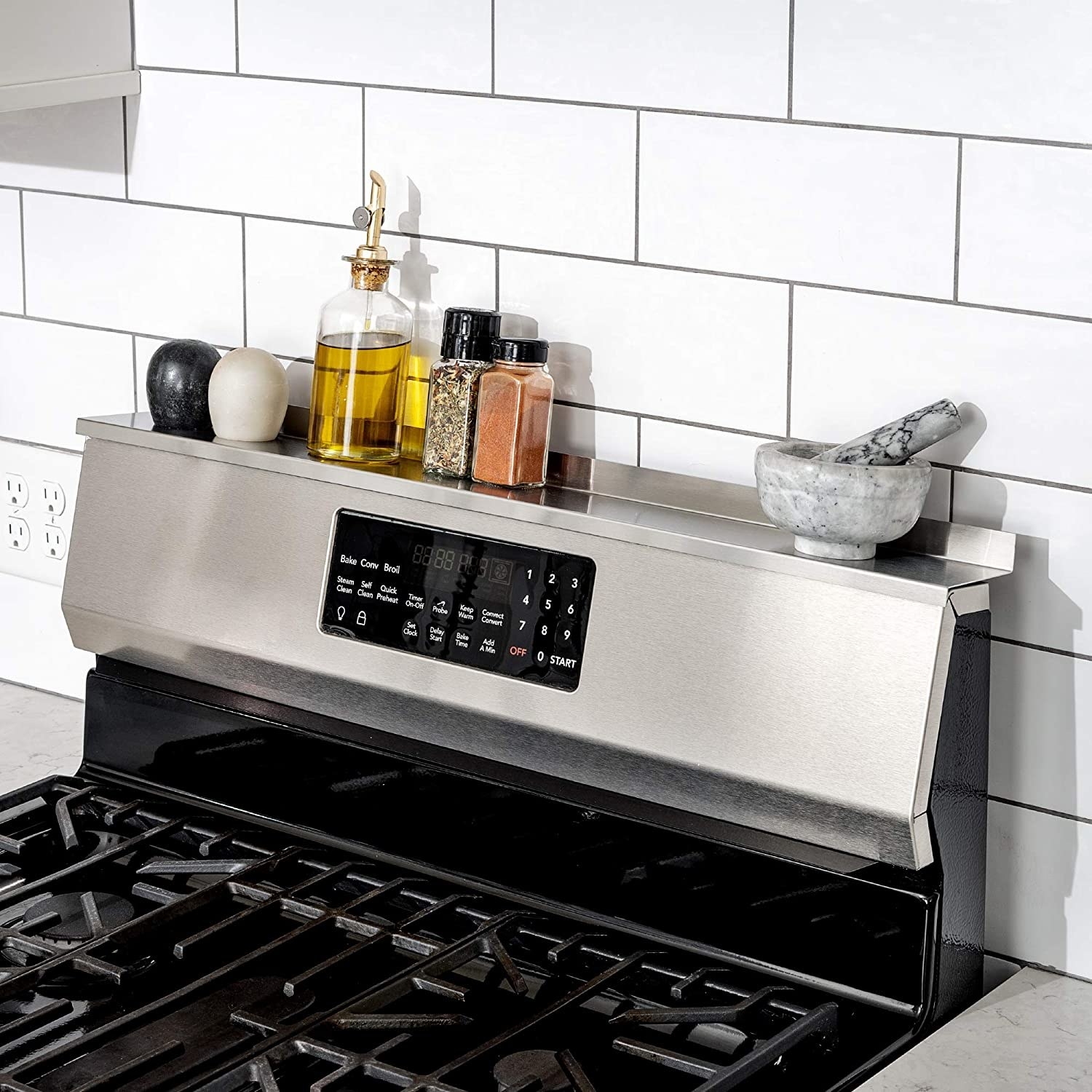 The shelf on top of the back of a stove range holding oil, salt and pepper shakers, other spices, and a mortar and pestle