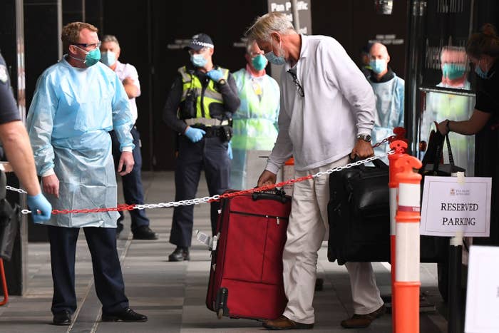A man with suitcases is greeted by a man in PPE at a hotel