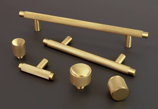 three knurled solid brass pulls and three knurled solid brass knobs on a black surface