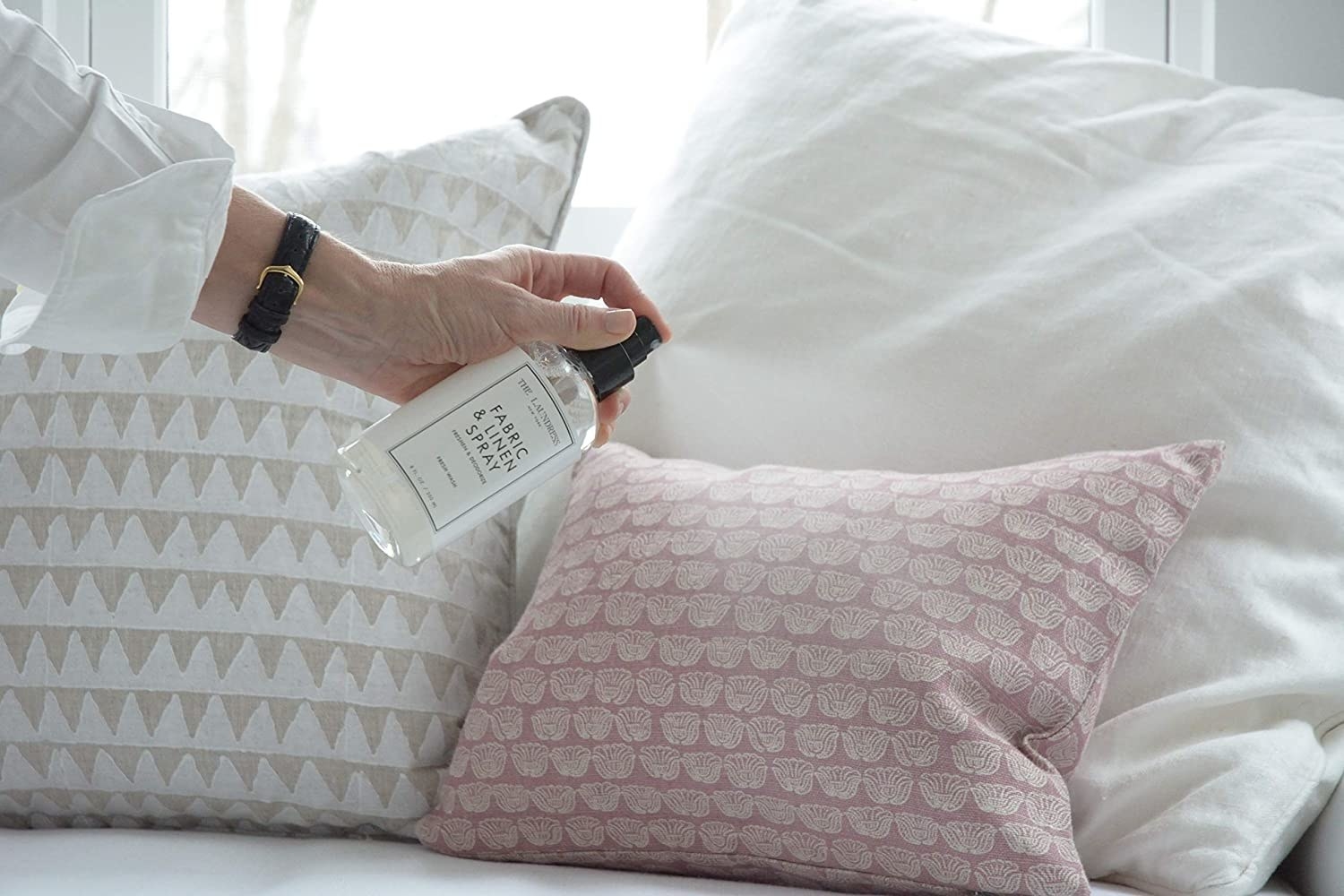 A person using the fabric spray onto a set of cushions