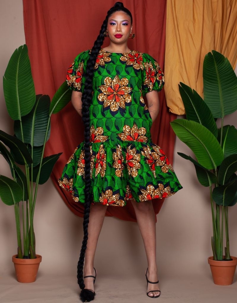 A model wearing the green, red, black and orange dress with short puff sleeves and a knee-length ruffle hem