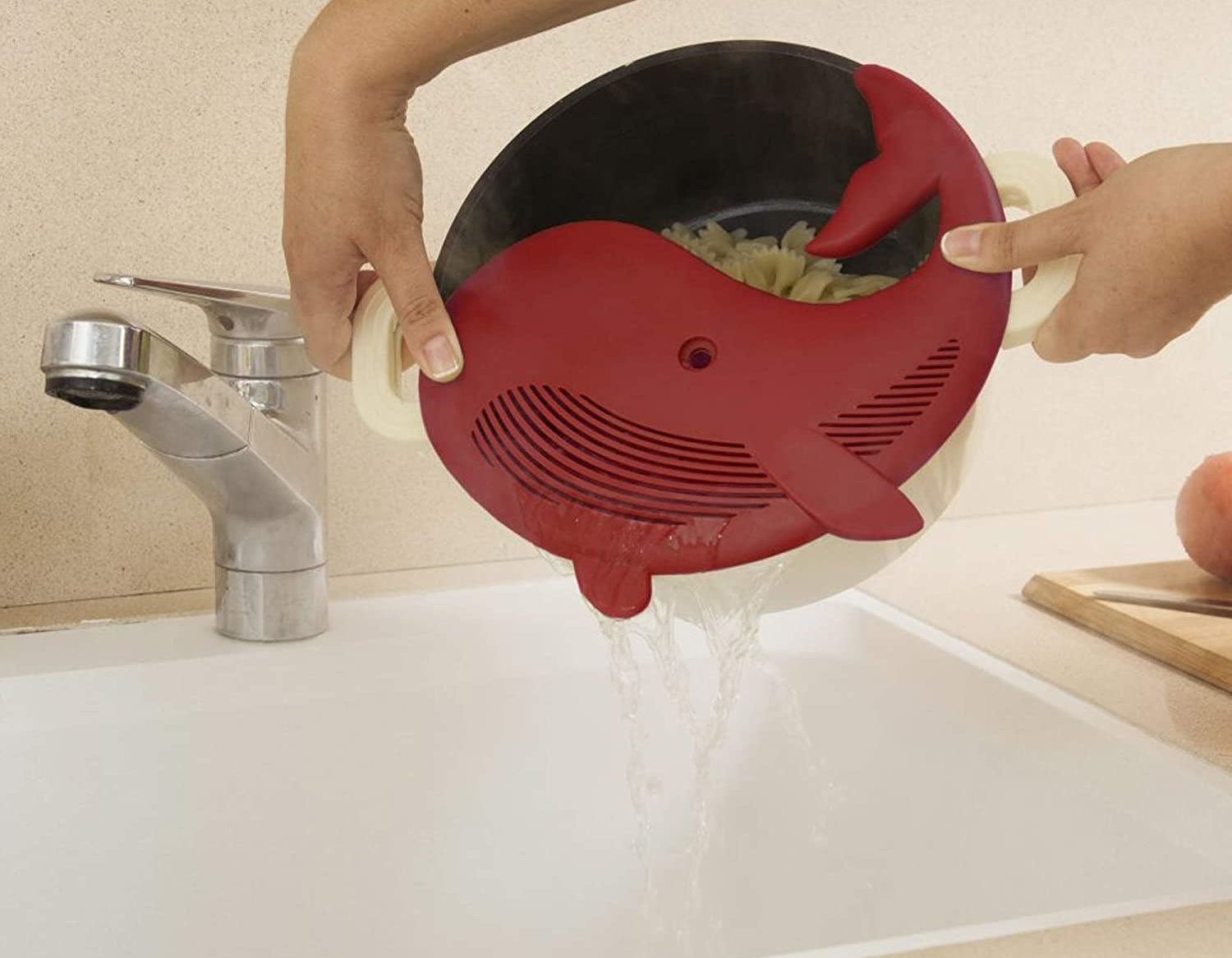 model holding a pot filled with pasta with a red whale-shaped strainer on top, getting the water out of the pot