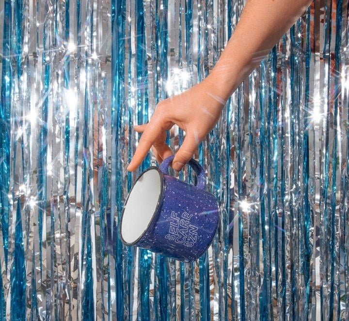 A person holding the mug that says self care season against a glittery background of streamers
