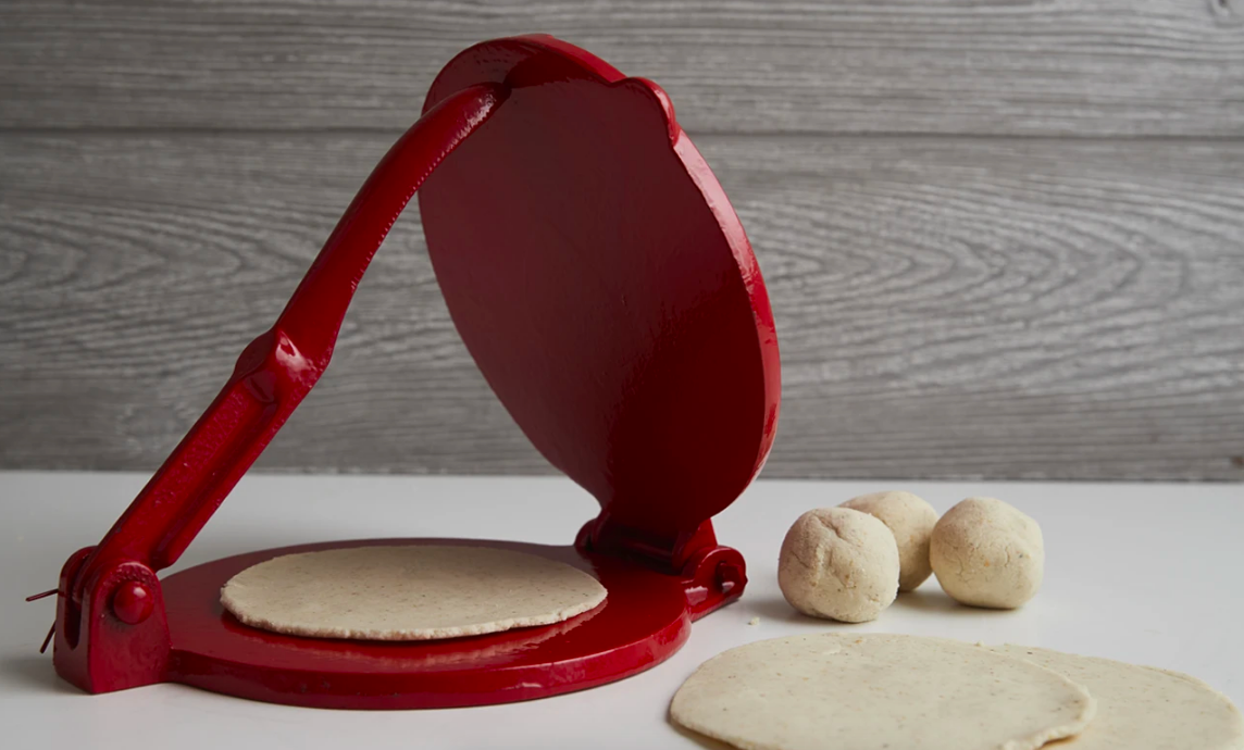 Bright red tortilla maker with balls of dough beside flat, finished pieces 