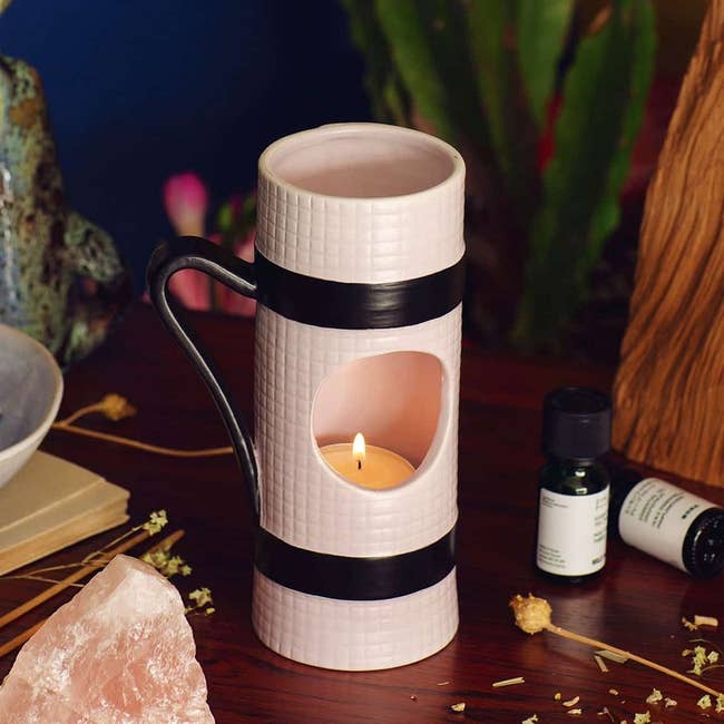 small tubular-shaped candle holder with hole in the middle, showing the candle inside made to look like a rolled-up yoga mat in white with black strap