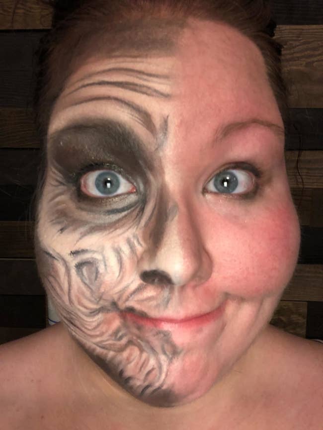 A reviewer wearing full-face Halloween makeup, with one side intact and the other side pretty much completely removed except for mascara