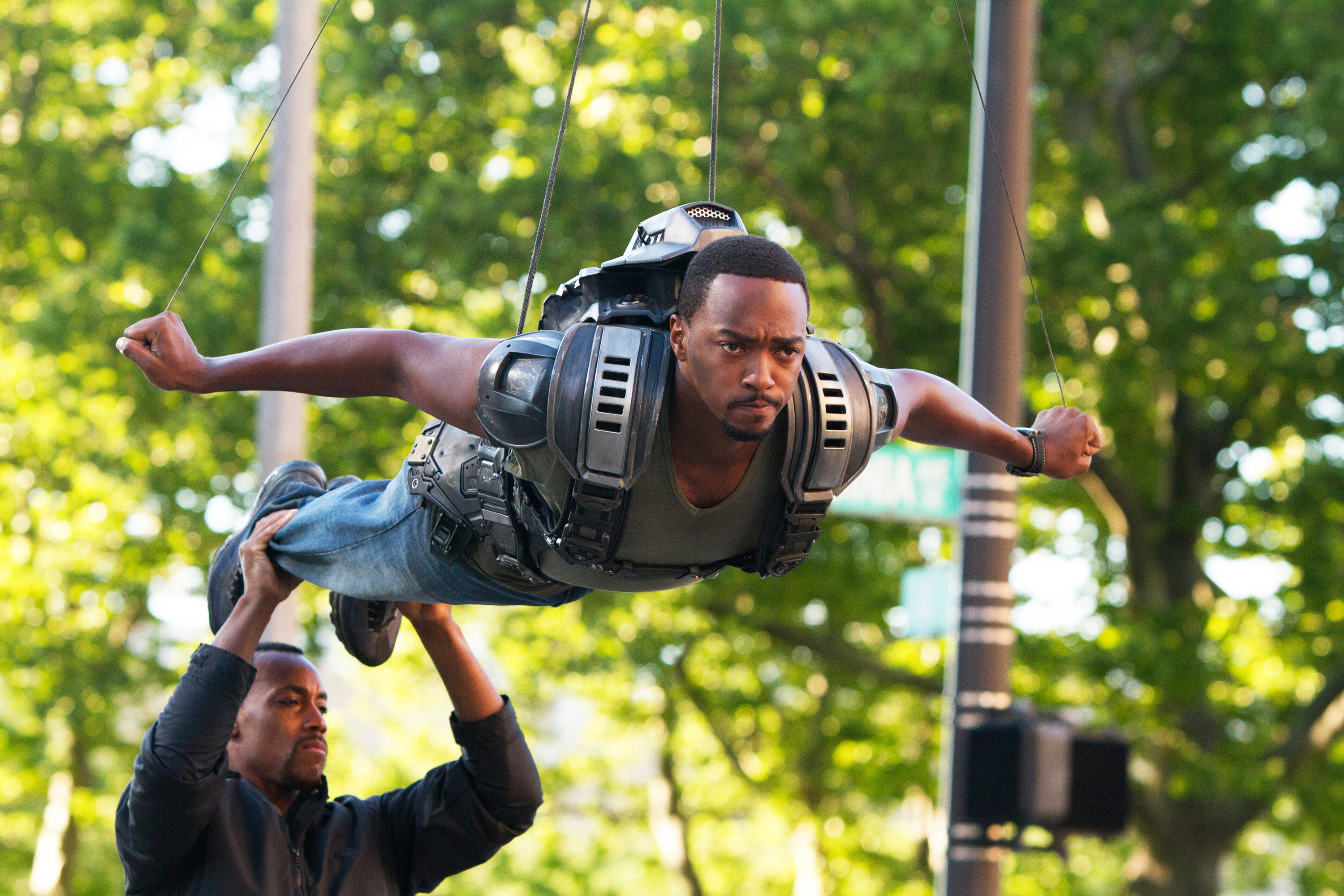 Anthony Mackie being held up by wire and pretending to fly as a man holds up his feet