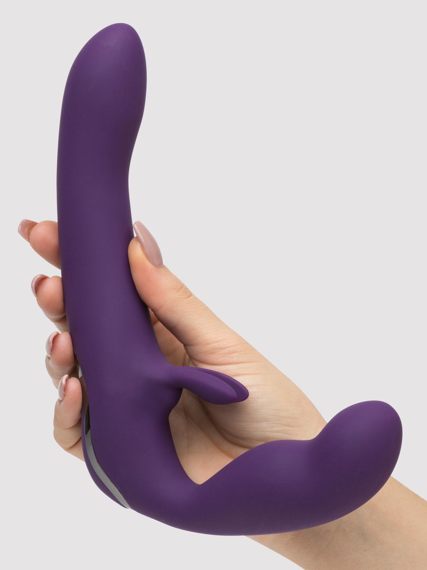 a hand holding the rechargeable strapless strap on which is purple and has rabbit ears for stimulation 