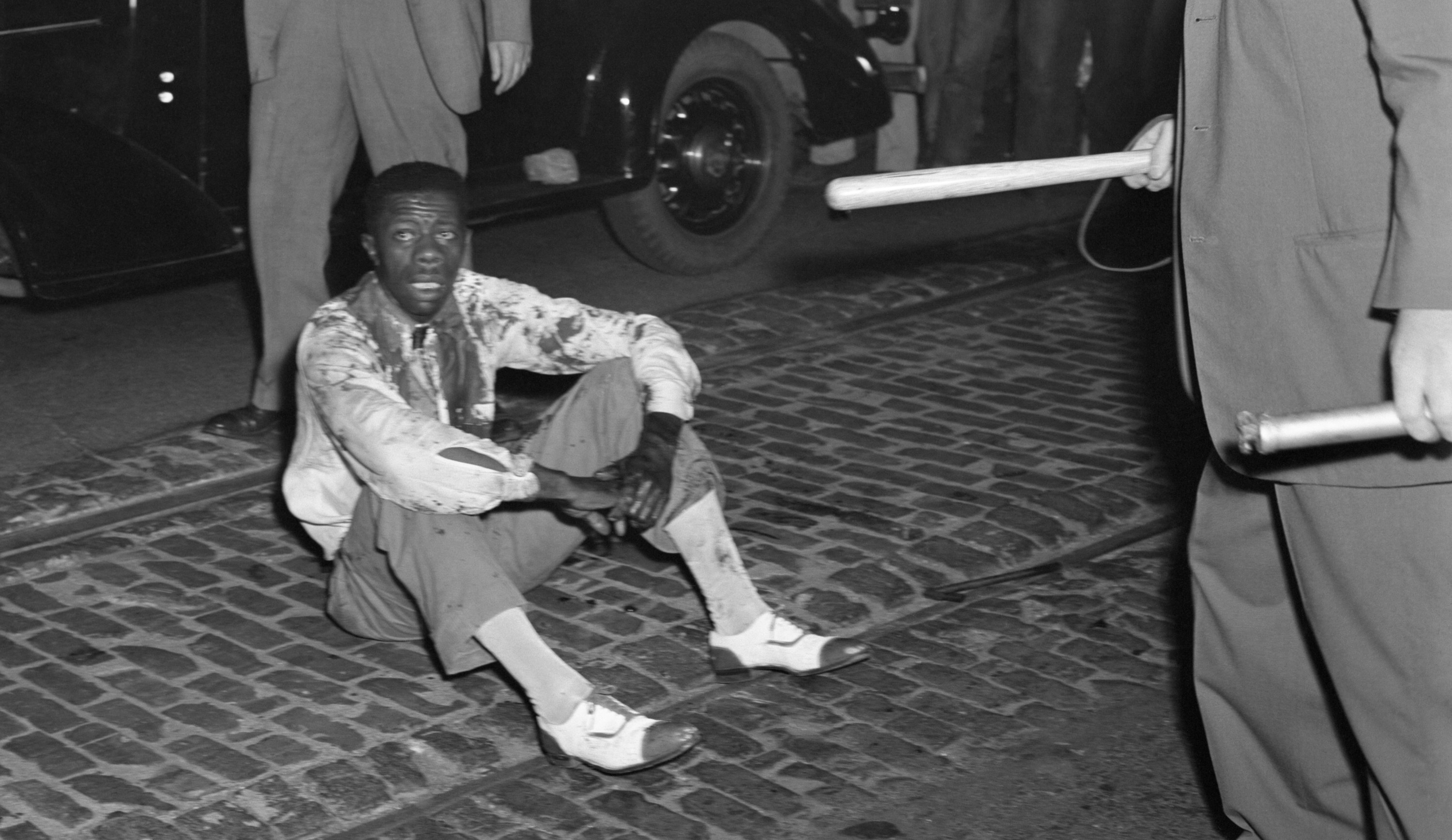 A Black man, whose clothes are soaked with his blood, sits on the street after being beaten and stoned by the mob during the St. Louis race riot