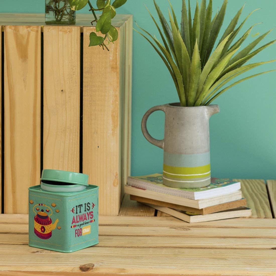 A teal jar that says "It's always time for chai" next to a plant 
