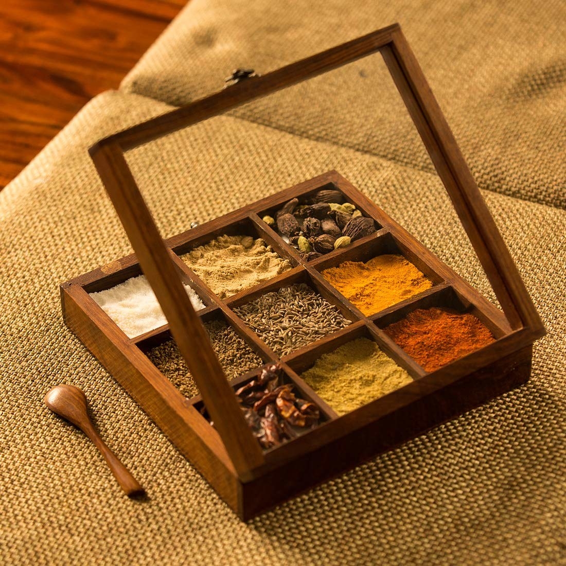 A Sheesham wood masala box with spices in it and a spoon beside it