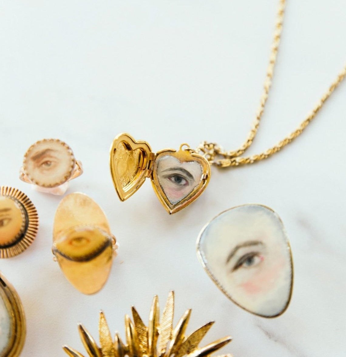 Several tiny gold necklaces, rings, and pendants with painted scenes and eyes 