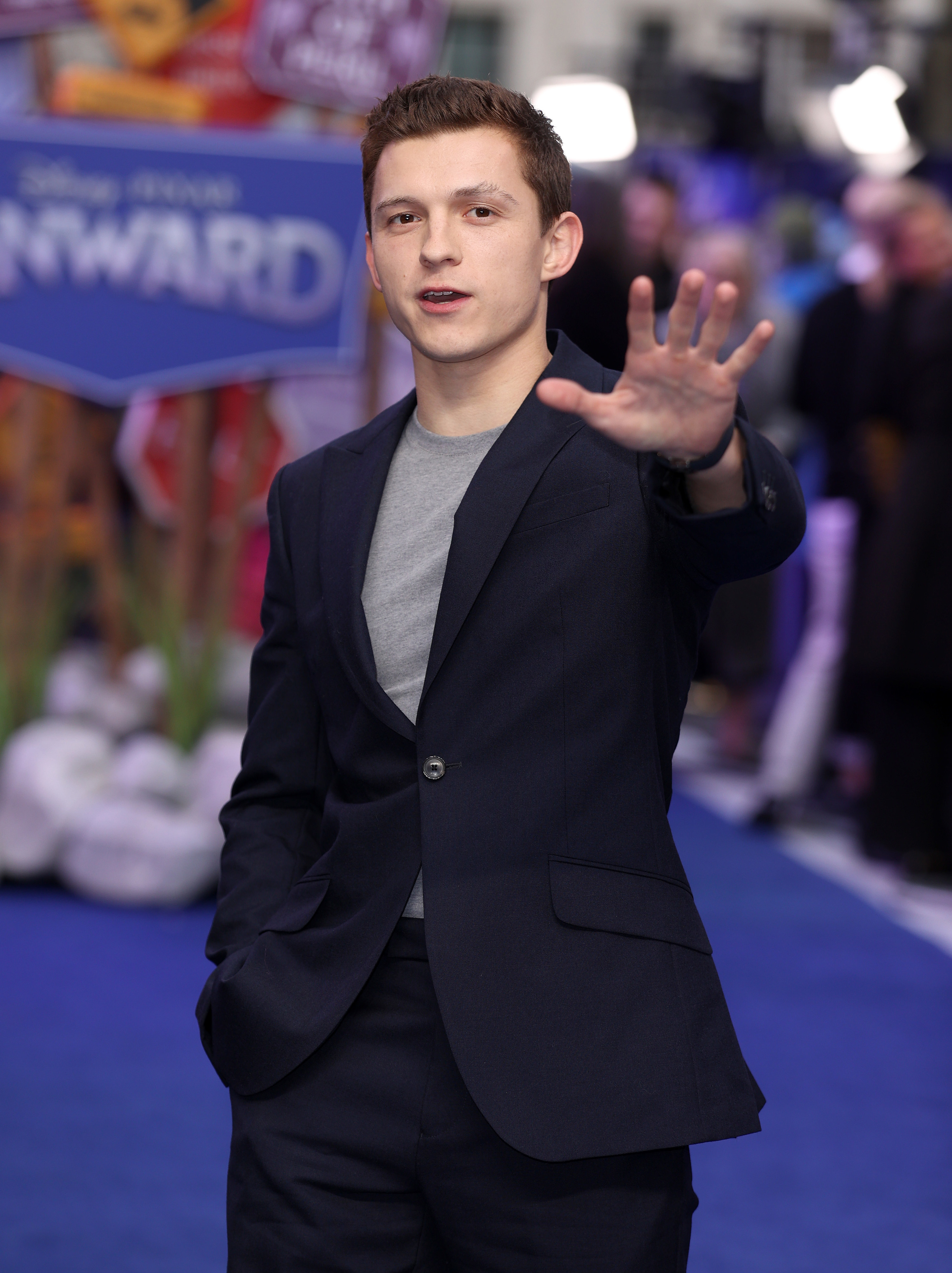 Tom Holland holding his arm up on the red carpet of a premier